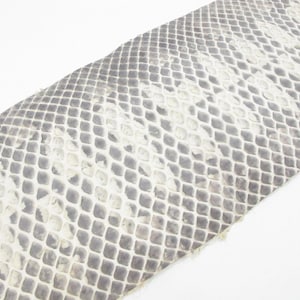 May include: A strip of textured material featuring a repeating diamond-shaped scale pattern in shades of grey, charcoal, and off-white. The surface displays a distinct, overlapping scale texture that mimics the appearance of natural snake skin.