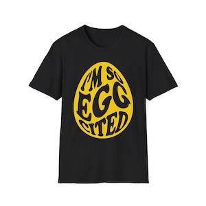 May include: Black t-shirt with a yellow egg graphic that reads "I'M SO EGG-CITED" in a playful font. The design is centered on the front of the shirt. The t-shirt is made of a soft material.
