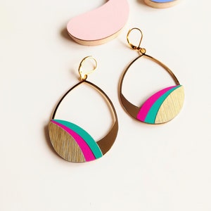 Peut inclure: Une paire de boucles d'oreilles pendantes dorées en forme de larme. Les boucles d'oreilles ont un motif rose et turquoise sur le bas.