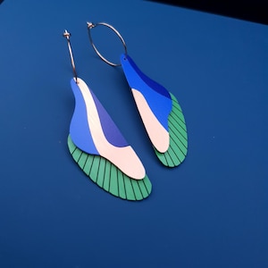 Peut inclure: Paire de boucles d'oreilles abstraites avec un design superposé. Elles présentent des formes bleues, blanches et vertes, avec un anneau doré. La couche inférieure est verte avec des lignes noires, et les couches supérieures sont bleues et blanches.