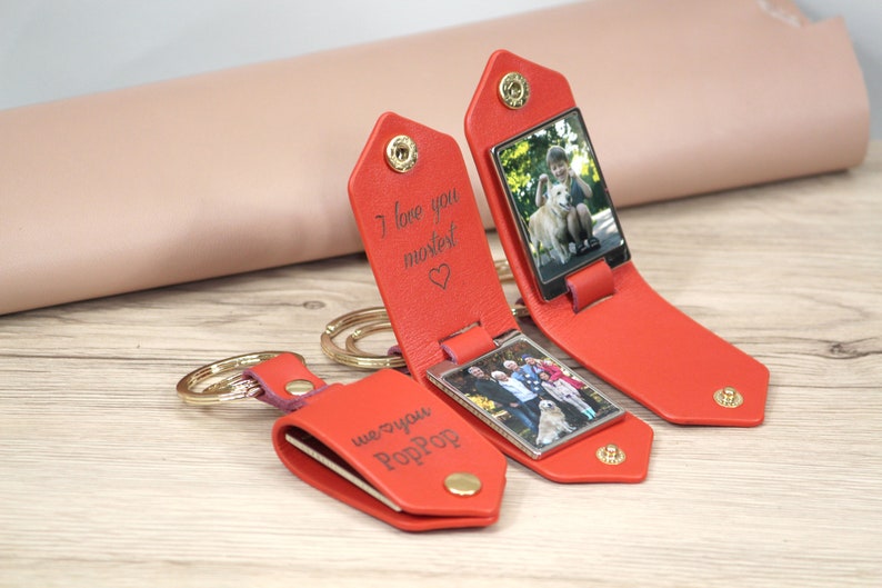 May include: Red leather keychains with a photo display. One keychain is open, revealing a photo of a person with a dog. The text "I love you mostest" is engraved on the keychain. Another keychain has the text "we ❤️ you PopPop".