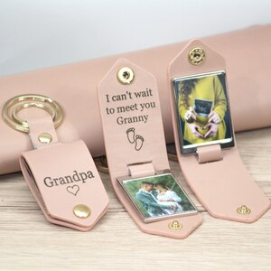 K&ouml;nnte beinhalten: Hellrosa Leder-Schl&uuml;sselanh&auml;nger mit goldenen Beschl&auml;gen. Ein Schl&uuml;sselanh&auml;nger mit der Aufschrift "Grandpa" mit Herz, ein weiterer mit "I can't wait to meet you Granny" mit Babyf&uuml;&szlig;en und der dritte mit einem Ultraschallbild.