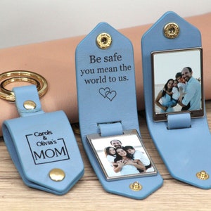 May include: Light blue leather keychain with a gold-colored key ring and snap closure. The keychain has a rectangular photo frame and the text "Be safe you mean the world to us." Another keychain has the text "Carols & Olivia's MOM".