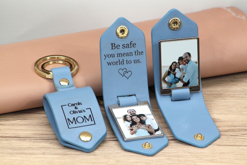 May include: Light blue leather keychain with a gold-colored key ring and snap closure. The keychain has a rectangular photo frame and the text "Be safe you mean the world to us." Another keychain has the text "Carols & Olivia's MOM".