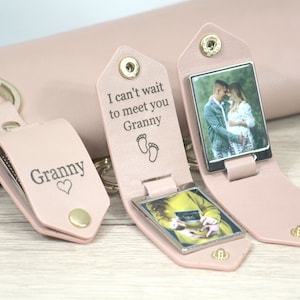 May include: Pink leather keychains with metal key rings. One keychain has the word "Granny" and a heart. Another keychain has the text "I can't wait to meet you Granny" with baby footprints. Both keychains have a photo inside.