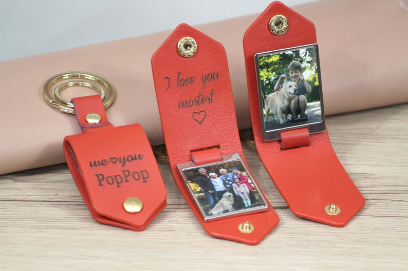 K&ouml;nnte beinhalten: Rote Leder-Schl&uuml;sselanh&auml;nger mit goldfarbener Hardware. Ein Schl&uuml;sselanh&auml;nger hat den Text "we love you PopPop". Zwei Schl&uuml;sselanh&auml;nger haben den Text "I love you mostest" und ein Foto. Ein Schl&uuml;sselanh&auml;nger hat ein Foto von einem Jungen und einem Hund.