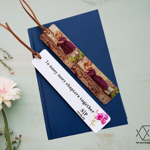 May include: White bookmark with the text "To many more chapters together SIP 02.25.25" and a watercolor illustration of pink flowers. The bookmark has a photo of a young girl in a purple dress on a tree branch.