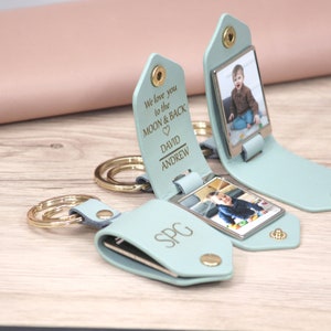 K&ouml;nnte beinhalten: Hellblaue Leder-Schl&uuml;sselanh&auml;nger mit goldfarbener Hardware. Jeder Schl&uuml;sselanh&auml;nger zeigt ein Foto und personalisierten Text: "We love you to the MOON & BACK" und Namen. Ein Schl&uuml;sselanh&auml;nger hat die Initialen "SPG". Die Schl&uuml;sselanh&auml;nger liegen auf einer Holzoberfl&auml;che.