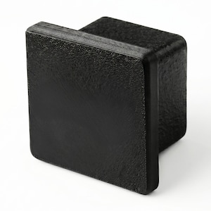 May include: A black, textured, square-shaped object with a handle. The object has a rough, grainy surface and rounded corners. The handle is a solid, rectangular piece. The item is likely a furniture component or a decorative element.