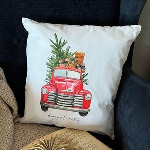 Könnte beinhalten: Roter Vintage-LKW mit einem Weihnachtsbaum und Geschenken auf der Ladefläche. Der LKW befindet sich auf einem weißen Kissen mit dem Text "Bringing home for Christmas".
