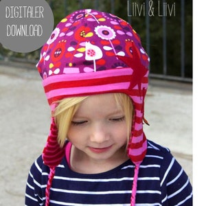 Könnte beinhalten: Ein Kind trägt eine rosa-rot gestreifte Mütze mit einem Blumenmuster und einem roten Stern an der Seite. Die Mütze hat lange Bänder, die ebenfalls rosa-rot gestreift sind. Das Kind trägt ein marineblaues und weiß gestreiftes Shirt.