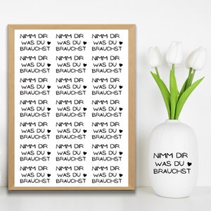 May include: A framed print with the German text "Nimm dir was du brauchst" in a repeating pattern. A white vase with the same text and a heart symbol is next to the print. White tulips are in the vase.