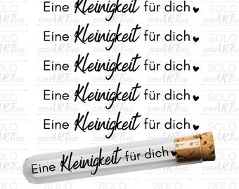 May include: A clear glass test tube with a cork stopper. The tube is filled with a small amount of cork and has the text "Eine Kleinigkeit für dich" written on it.