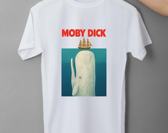 May include: White t-shirt featuring a graphic of a white whale with a ship above it and the text "MOBY DICK" in red. The whale is set against a blue background, creating a nautical theme.