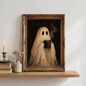 May include: A framed wall art print featuring a beige ghost figure draped in fabric, holding a black mug with rising steam against a dark background. The artwork is enclosed in an ornate, antique-style gold frame with intricate carved detailing.