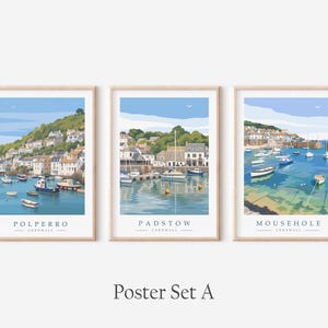 May include: A set of three vertical posters featuring illustrations of the coastal towns of Polperro, Padstow, and Mousehole in Cornwall. Each print depicts a harbor scene with boats on blue water, hillside buildings, and the town name printed below.