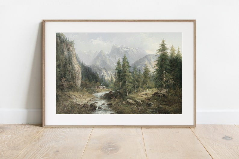 May include: A framed painting depicting a mountain landscape with a river flowing through a forest. The mountains are snow-capped and the trees are green. A small cabin is visible in the distance.