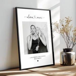 K&ouml;nnte beinhalten: Schwarzwei&szlig;foto von zwei Frauen, einer Mutter und ihrer Tochter, die l&auml;cheln und in die Kamera schauen. Das Foto ist in einem schwarzen Rahmen mit einem wei&szlig;en Passepartout gerahmt. Der Text "Olivia & Mum" steht &uuml;ber dem Foto, und der Text "Eine Mutter ist die beste Freundin ihrer Tochter" steht unter dem Foto.
