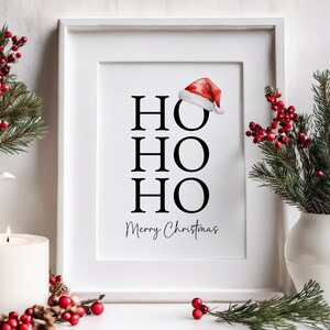 May include: White framed print with the text "HO HO HO Merry Christmas" in black lettering. A red Santa hat is above the text.