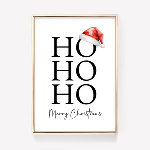 May include: A white printable art print with a gold frame. The print features the words "HO HO HO" in black text and the words "Merry Christmas" in cursive text. A red and white Santa hat is at the top of the print.