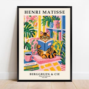 Könnte beinhalten: Ein gerahmter Kunstdruck mit einer Illustration einer Katze, die ein Buch liest und eine Brille trägt. Die Katze liegt auf einem rosa Kissen, umgeben von Pflanzen und Büchern. Der Druck enthält den Text "HENRI MATISSE" und "BERGGRUEN & CIE", mit Pariser Adresse.