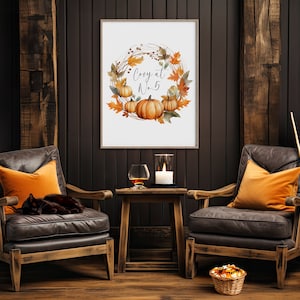 Pode incluir: Uma impress&atilde;o emoldurada com uma coroa de aquarela de folhas de outono e ab&oacute;boras. O texto "Cozy at Home" est&aacute; no centro da coroa. A impress&atilde;o est&aacute; pendurada em uma parede de madeira escura. Duas poltronas de couro com almofadas laranja est&atilde;o em frente &agrave; impress&atilde;o. Uma vassoura est&aacute; encostada na parede &agrave; direita das poltronas.