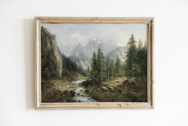 May include: A framed oil painting depicting a mountain landscape with a river flowing through a forest. The painting features a small cabin in the distance and a cloudy sky.