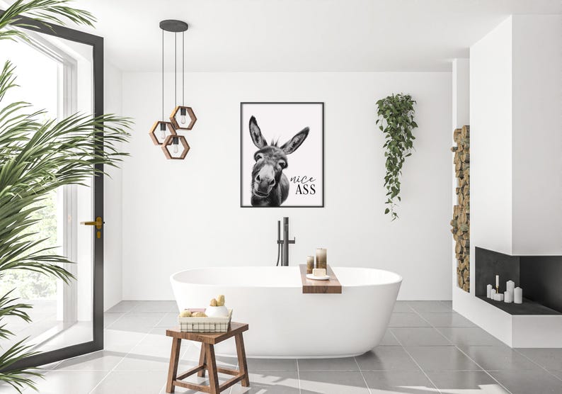 K&ouml;nnte beinhalten: Ein schwarz-wei&szlig; gerahmter Druck eines Esels mit dem Text "nice ass" in einem modernen Badezimmer. Das Badezimmer verf&uuml;gt &uuml;ber eine wei&szlig;e Badewanne, einen Holzschemel und eine H&auml;ngepflanze. Der Raum ist hell und luftig.