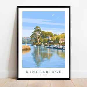 May include: A framed travel poster print featuring a scenic view of Kingsbridge, Devon. The illustration depicts a calm blue estuary with several moored white boats, green hills, trees, and buildings under a clear sky. The text reads KINGSBRIDGE DEVON.