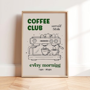 May include: A framed print with a beige background and a coffee theme. The words "COFFEE CLUB" are in green above a black line drawing of an espresso machine. Below the machine, the words "every morning" and "7am - 10am" are in green.