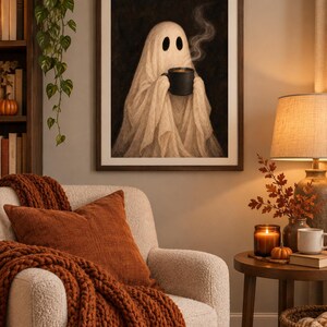 May include: A framed wall art print featuring a white ghost draped in a sheet, holding a black mug with rising steam. The ghost has two large, dark, oval-shaped eyes and is set against a dark, textured background within a simple brown frame.