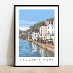 May include: A framed art print featuring a colorful illustration of Bayard's Cove in Dartmouth. The scene depicts a waterfront with light-colored buildings, a stone quay, small boats on blue water, and green hills under a clear blue sky.