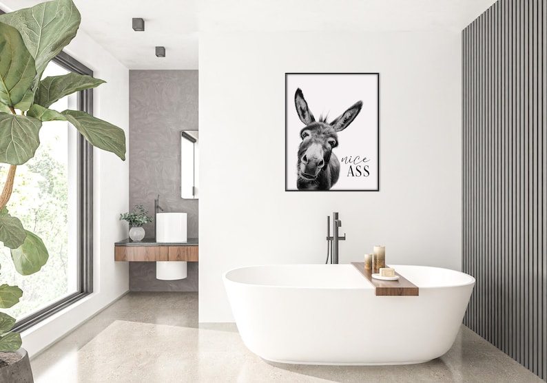 K&ouml;nnte beinhalten: Schwarz-wei&szlig; gerahmter Kunstdruck mit einem Esel und dem Text "nice ASS". Das Kunstwerk wird in einem modernen Badezimmer mit einer wei&szlig;en Badewanne, Kerzen und einer gro&szlig;en gr&uuml;nen Pflanze ausgestellt.