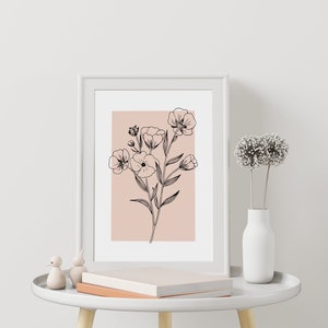Pode incluir: Uma impress&atilde;o emoldurada branca com um desenho de linha preta de flores sobre um fundo rosa claro. A impress&atilde;o est&aacute; sobre uma mesa auxiliar branca com um livro e duas pequenas figuras de p&aacute;ssaros.
