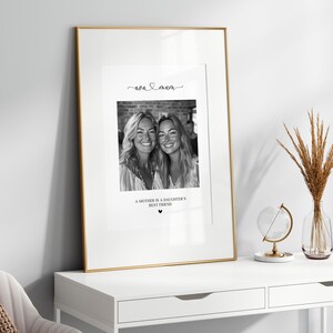 K&ouml;nnte beinhalten: Schwarzwei&szlig;foto von zwei Frauen, einer Mutter und ihrer Tochter, mit dem Text "Eine Mutter ist die beste Freundin ihrer Tochter" und einem Herzsymbol unter dem Foto. Das Foto ist in einem goldenen Rahmen gerahmt und steht auf einem wei&szlig;en Tisch.