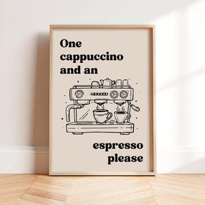 Op de afbeelding: Een ingelijste print met een zwart-wit illustratie van een espressomachine. De tekst luidt "One cappuccino and an espresso please". Het kunstwerk staat tegen een beige achtergrond, met een licht houten frame.