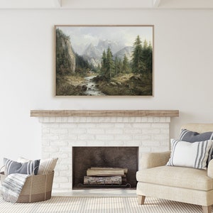 May include: A framed landscape painting of a mountain scene with a river flowing through a forest. The painting is in a light wood frame and is hanging above a white brick fireplace.