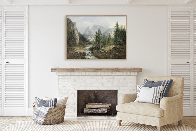 May include: A framed landscape painting of a mountain scene with a river flowing through a forest. The painting is in a light wood frame and is hanging above a white brick fireplace.
