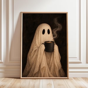 May include: A framed wall art print featuring a beige ghost draped in fabric, holding a black mug with steaming hot liquid. The ghost has two dark oval eye holes and is set against a dark, textured background within a light wood frame.
