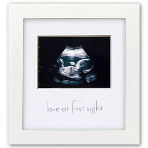 May include: A white framed print featuring a black and white ultrasound image of a baby. The text "love at first sight" is printed in a delicate script below the image. The frame is square.