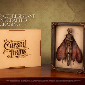 Fairy shadow box next to branded wooden Cursed Items shipping box.