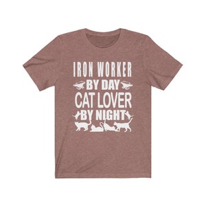 May include: A heather brown t-shirt with the text "Iron Worker By Day Cat Lover By Night" in white. The text is surrounded by images of cats and an anvil.