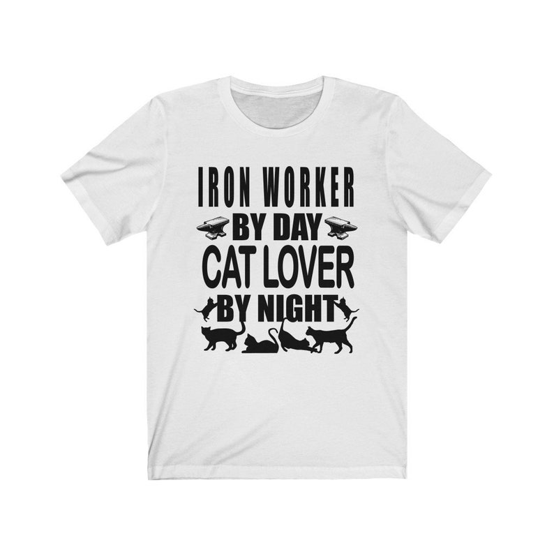 May include: White t-shirt with black text that reads "Iron Worker By Day Cat Lover By Night". The text is surrounded by images of cats and an anvil.