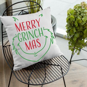 May include: White throw pillow with green and red text that reads "Merry Grinch Mas" in a whimsical font. The pillow is sitting on a black metal chair.