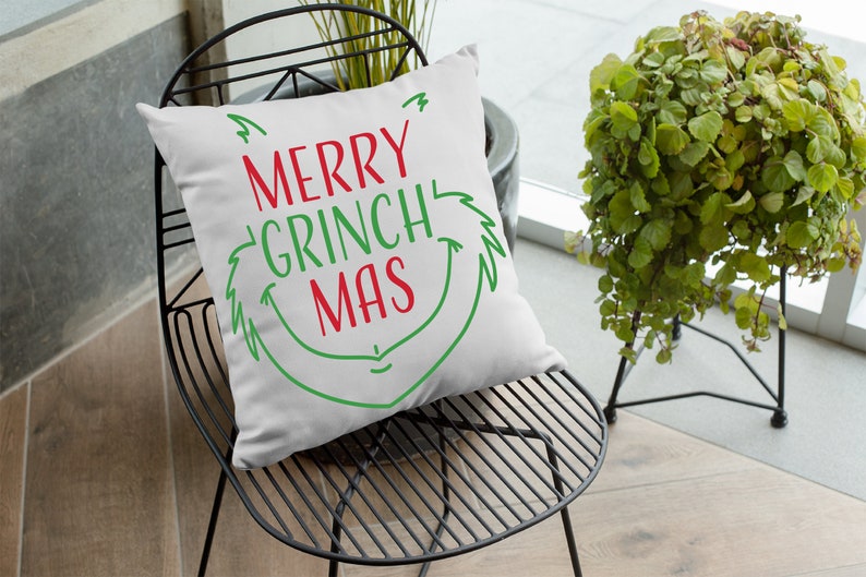 May include: White throw pillow with green and red text that reads "Merry Grinch Mas" in a whimsical font. The pillow is sitting on a black metal chair.