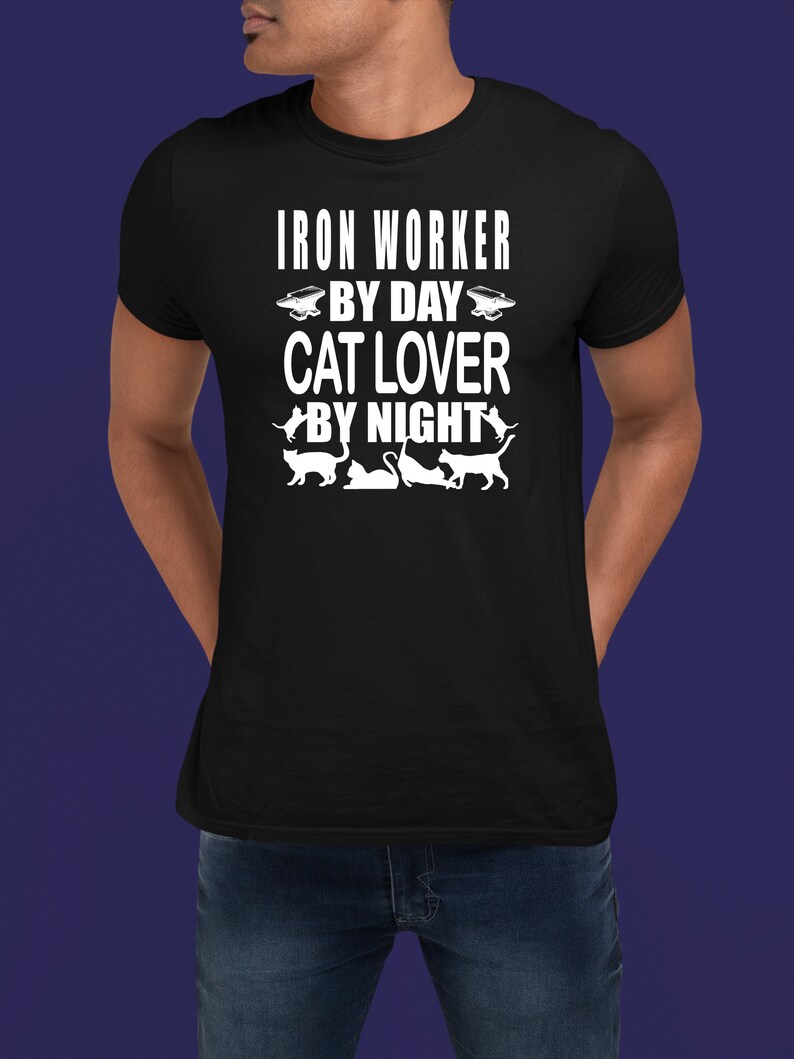 May include: A black t-shirt with white text that reads "Iron Worker By Day Cat Lover By Night". The shirt features a silhouette of an anvil and several cats.