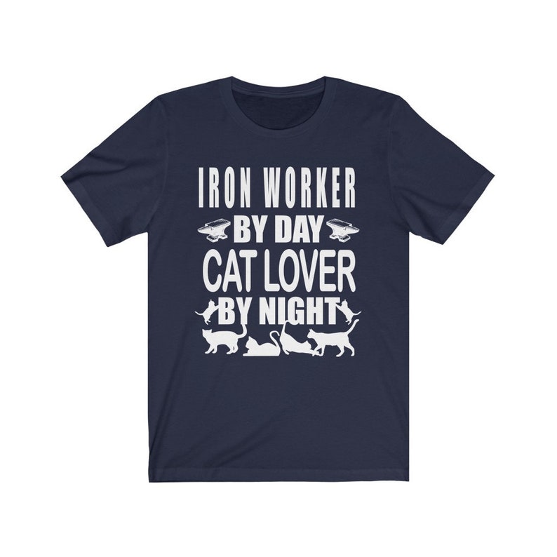 May include: Navy blue t-shirt with white text that reads "Iron Worker By Day Cat Lover By Night". The shirt features a silhouette of a cat and an anvil.