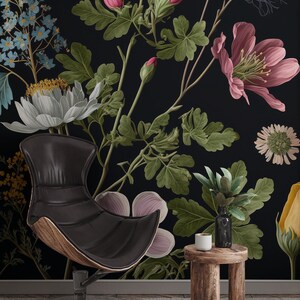 May include: A black leather chair with a wooden base sits in front of a black wall with a floral wallpaper featuring pink, white, and green flowers. A small wooden stool with a white cup sits next to the chair.