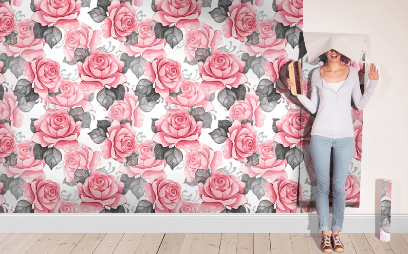 Puede incluir: Una mujer est&aacute; colocando papel tapiz floral rosa y gris con un dise&ntilde;o de acuarela en una pared. El papel tapiz presenta un patr&oacute;n repetitivo de rosas rosas y hojas grises.