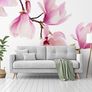 May include: A white couch with a green throw blanket sits in a room with a white wall featuring a pink magnolia flower mural. A small potted plant and a floor lamp are also in the room.